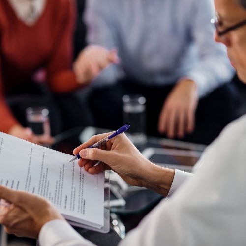 Close-up of insurance agent analyzing an agreement while having consultations with clients in the office.